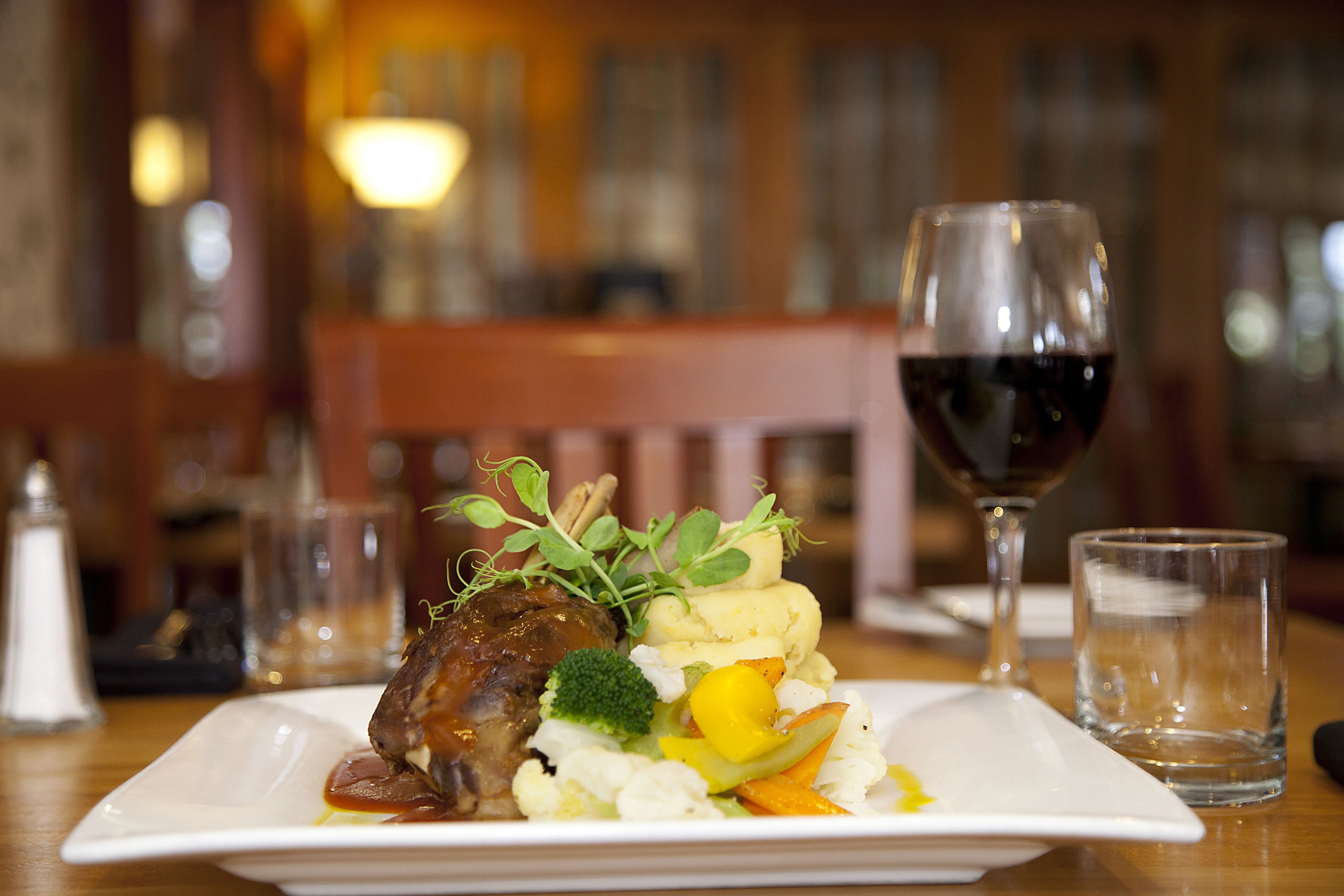 A plate of food with a glass of red wine and a glass of water on a wooden table.