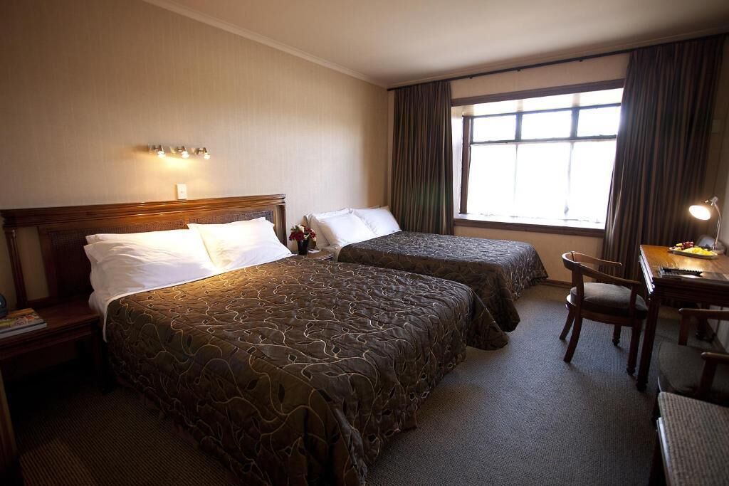 A hotel room with two beds, a desk, and a chair.