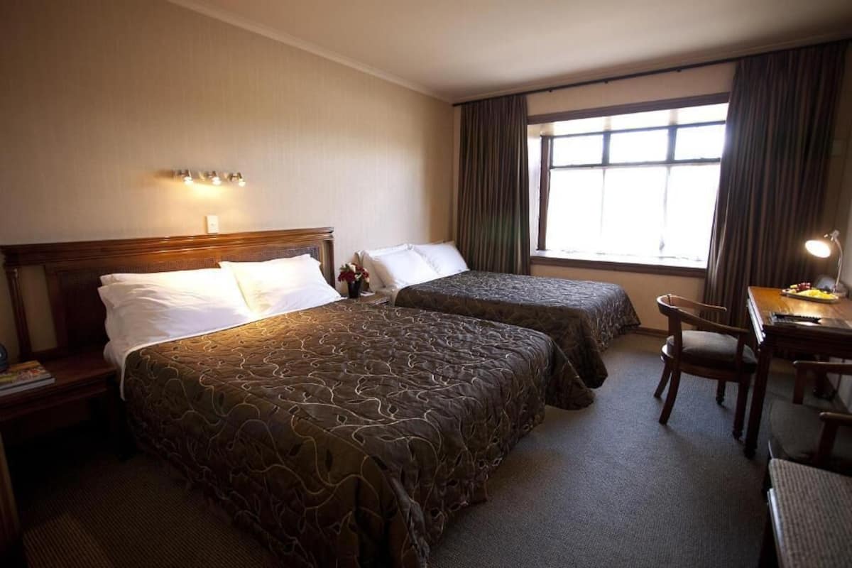A hotel room with two beds, a desk, and a chair.