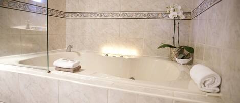 A bathroom with a large bathtub, a glass-enclosed shower, and a decorative tile border.