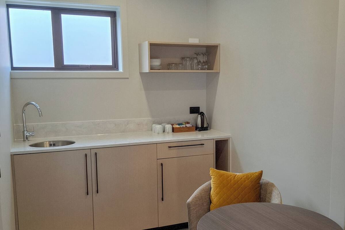 A compact kitchen with a window, a sink, a countertop, and a small dining area with a table and a chair.
