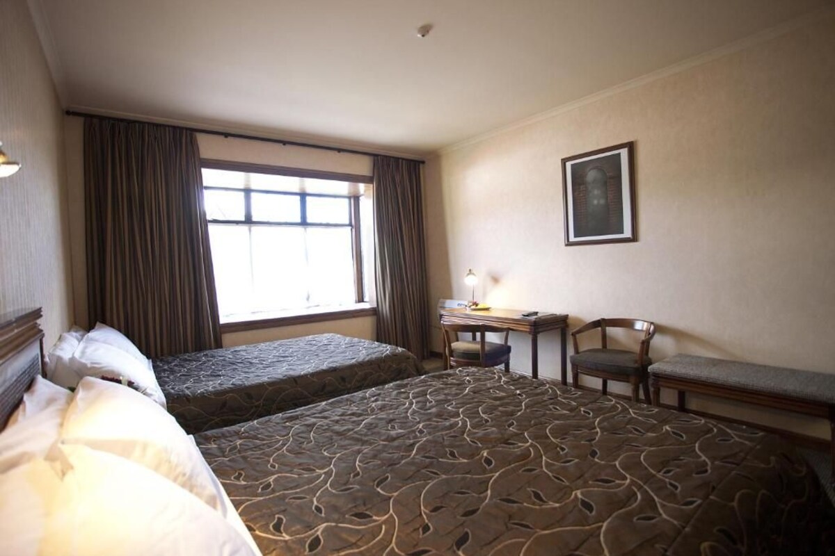 A hotel room with two beds, a desk, a chair, and a window with curtains.