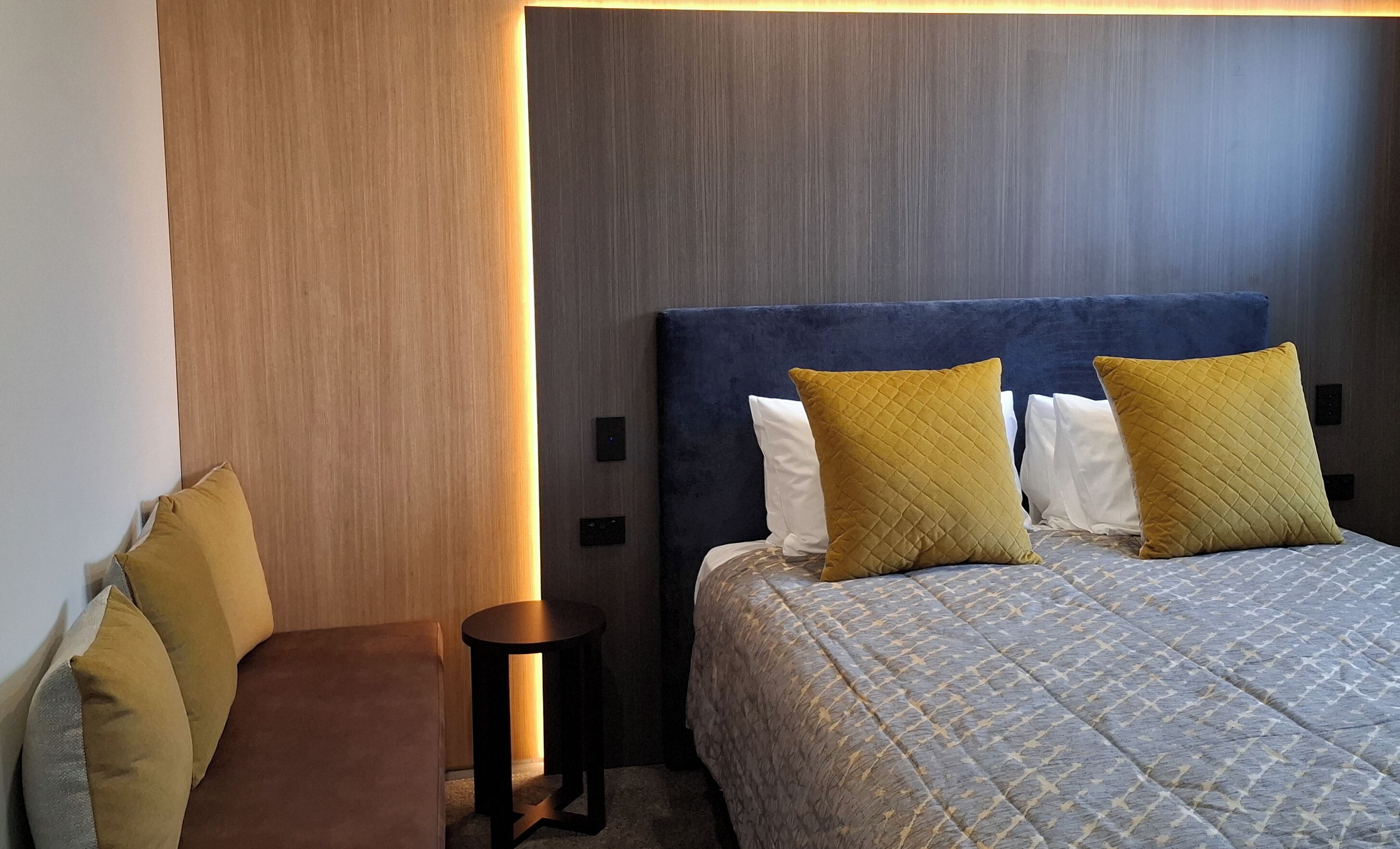 Hotelkamer met een bed, twee kussens, een nachtkastje en een muur met lichtschakelaar.