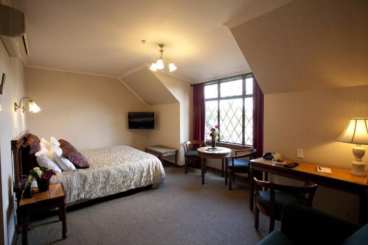 A hotel room with a bed, desk, chair, and a TV mounted on the wall.