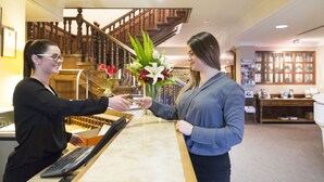 A reception desk with a keyboard, a vase with flowers, and a staircase in the background. - Distinction Coachman Hotel, Palmerston North (Palmerston North)