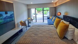 A hotel room with a large bed, a TV, a sofa, and a dining area with a table and chairs. - Distinction Coachman Hotel, Palmerston North (Palmerston North)
