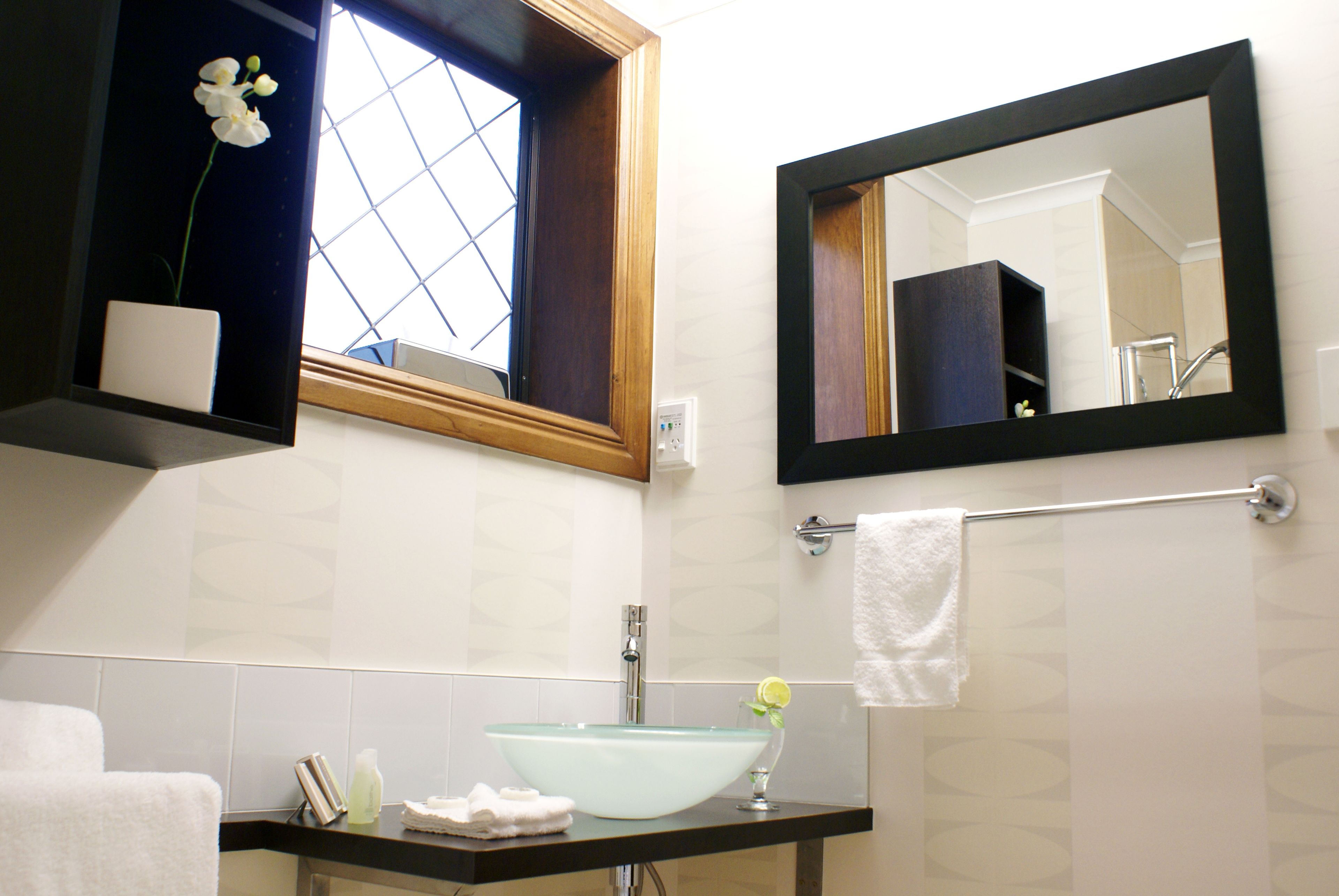 A bathroom with a glass sink, a mirror, a window, and a towel rack.