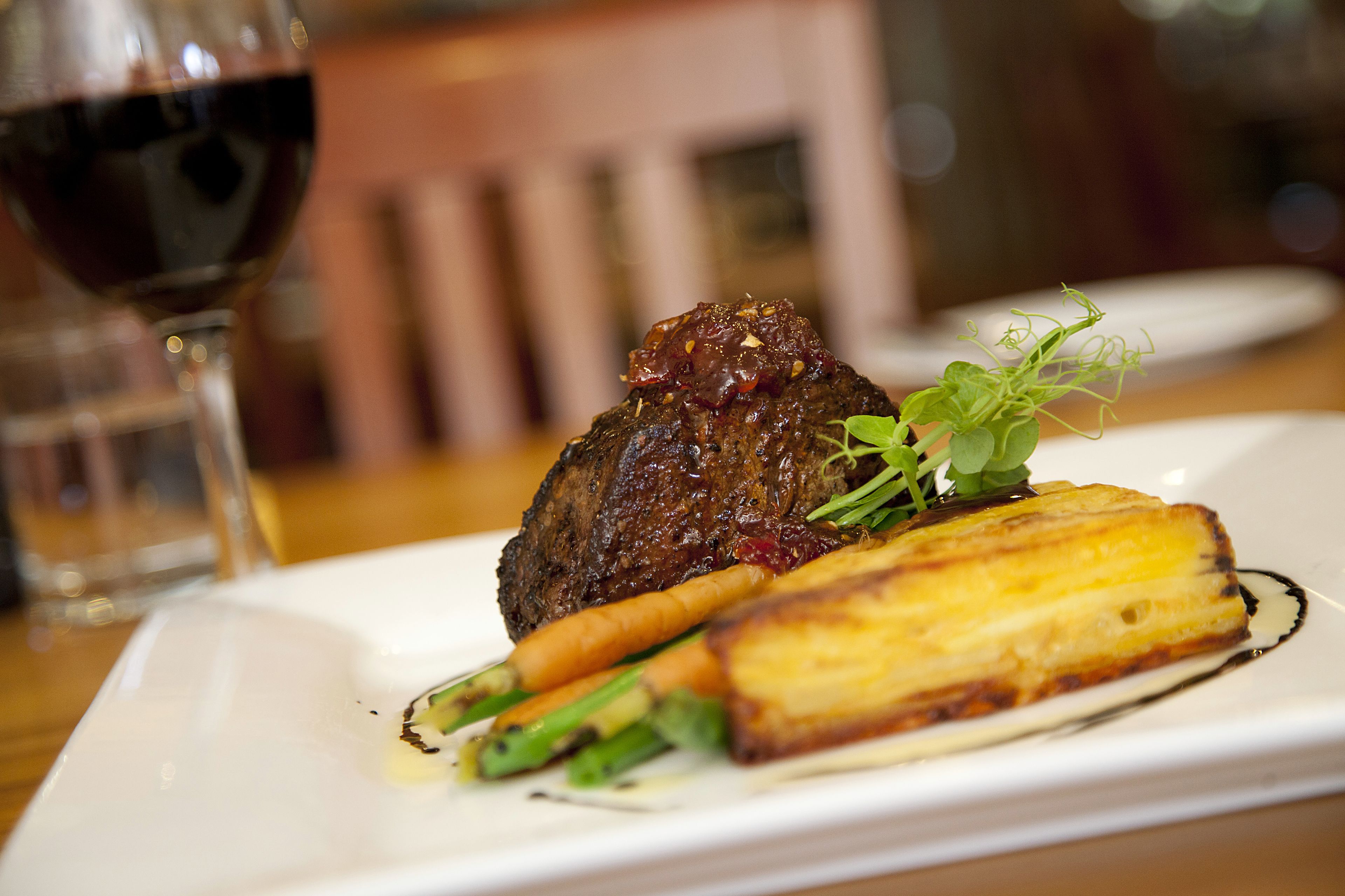 Ein angerichtetes Gericht mit einem Steak, Gemüse und einem Glas Rotwein.