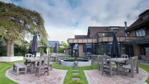An outdoor patio area with tables and chairs, a central fountain, and a building in the background. - Distinction Coachman Hotel, Palmerston North (Palmerston North)