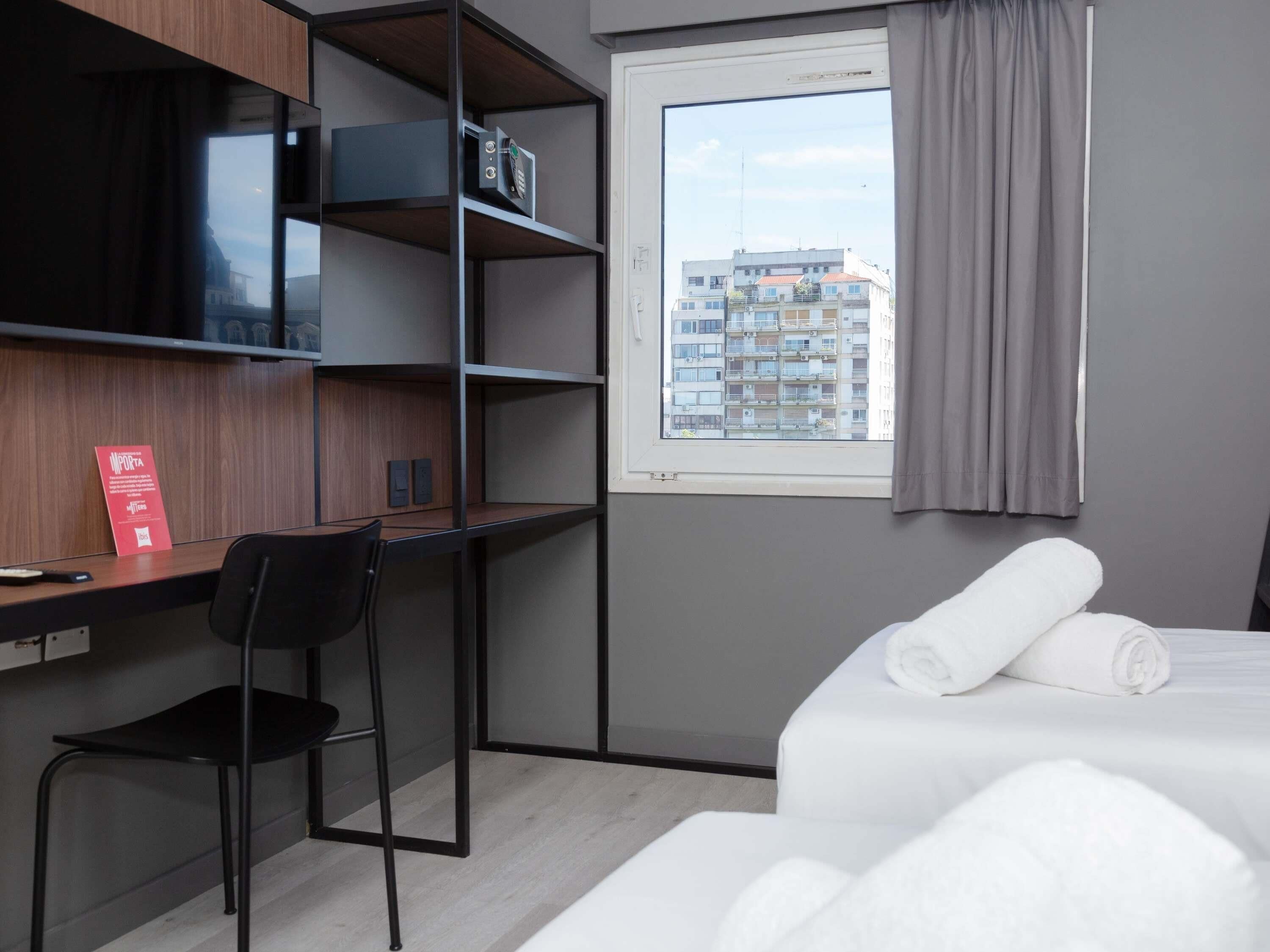 Habitación de hotel con escritorio, silla, cama y ventana con cortinas.