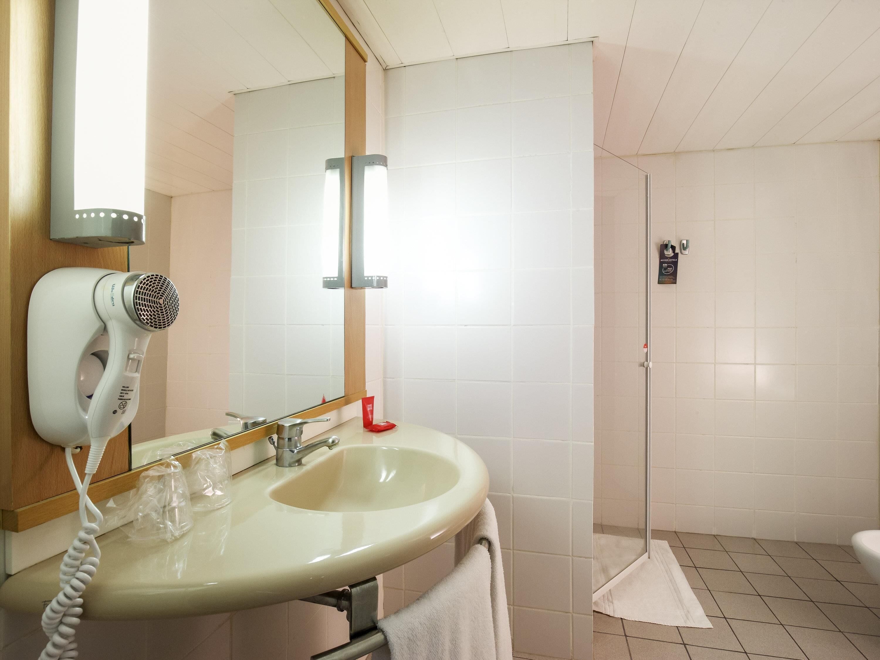 Un baño con lavamanos, secador de pelo, espejo y zona de ducha.