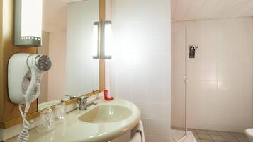 A bathroom with a sink, a hairdryer, a mirror, and a shower area.