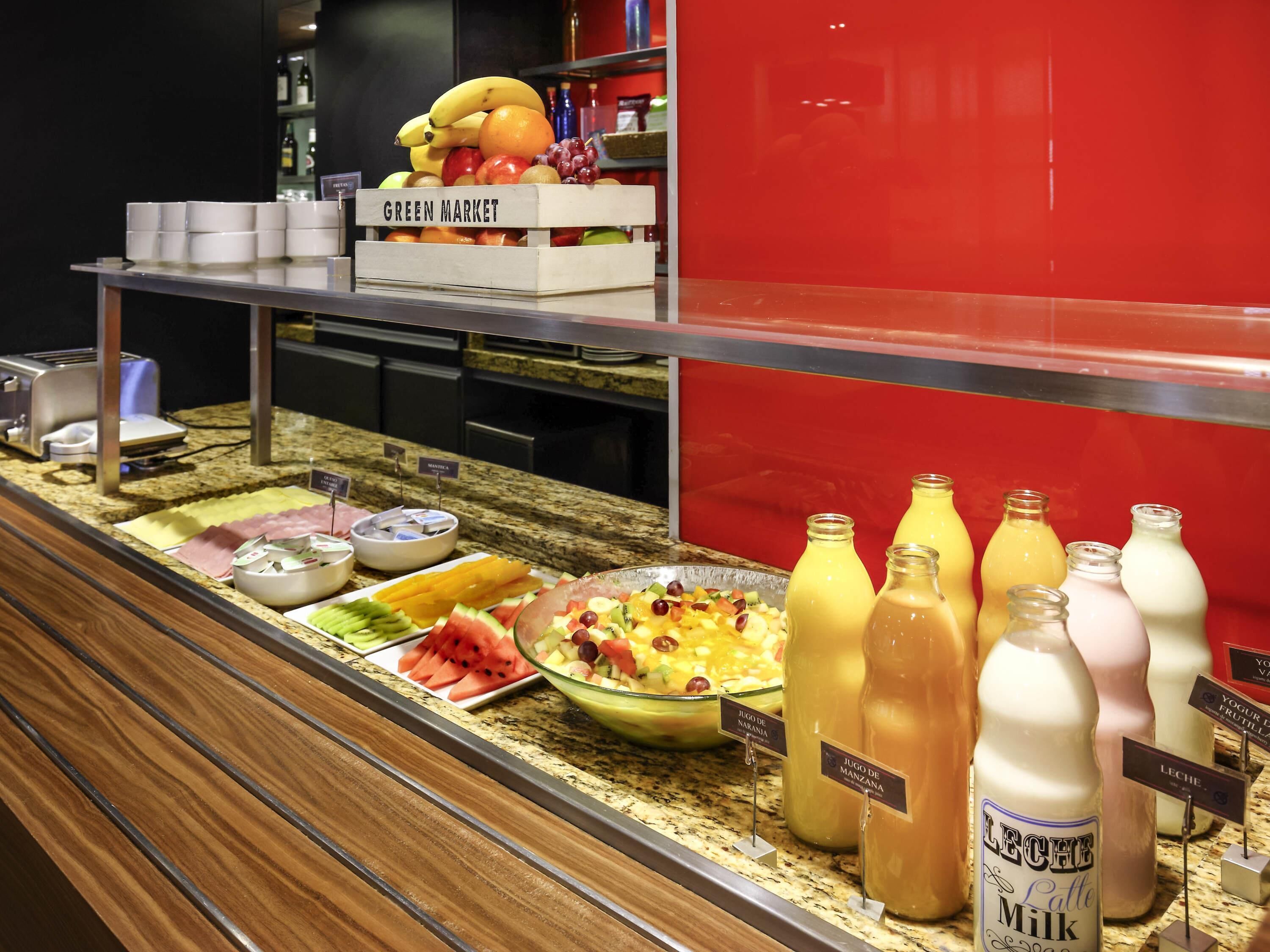 A buffet with various food and drink options, including a green market section with fruits and a juice bar with labeled beverages.
