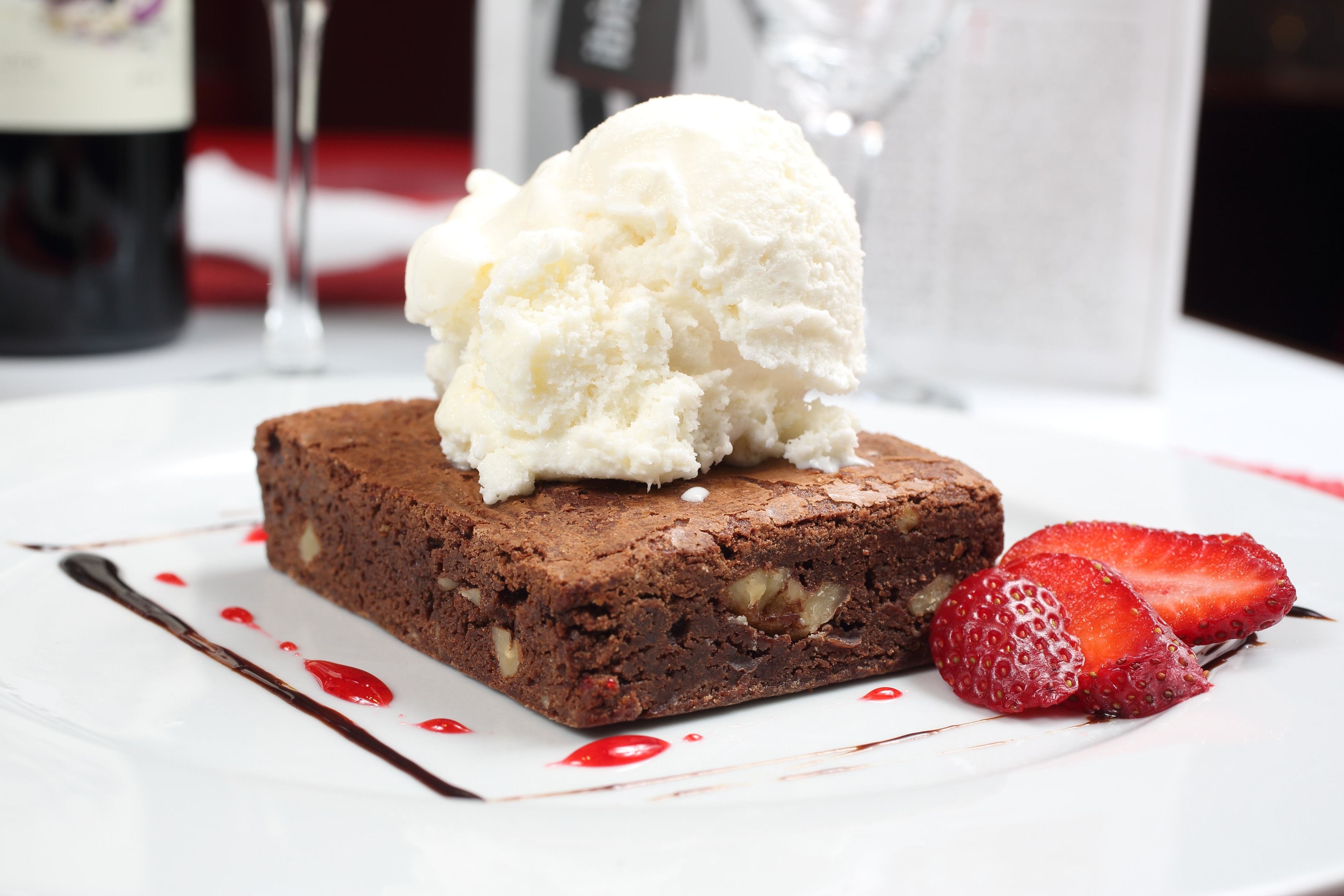 A dessert plate with a brownie, a scoop of vanilla ice cream, and a strawberry.