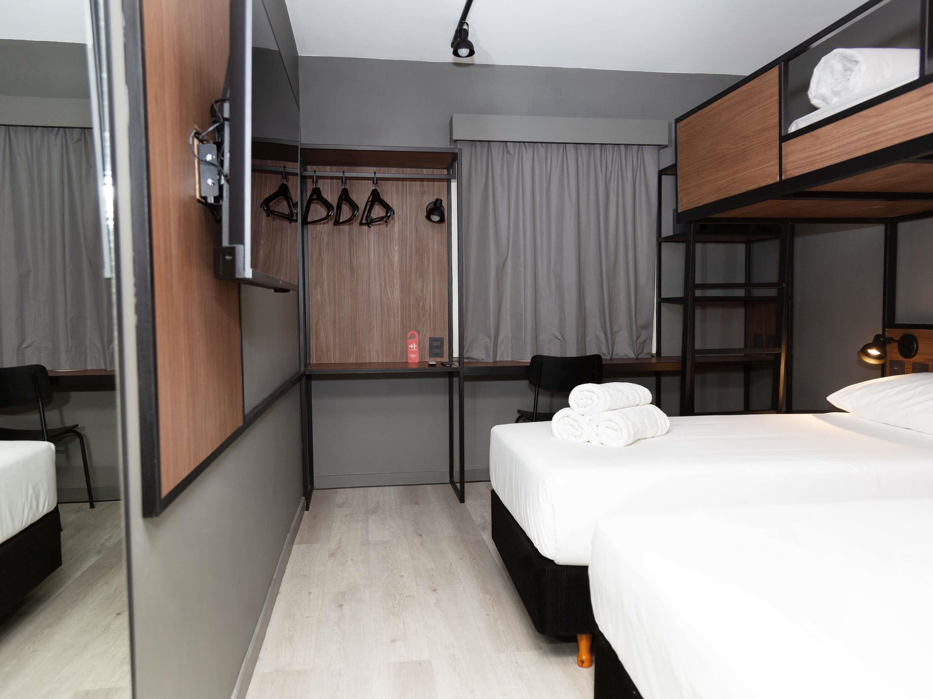 A hotel room with a bunk bed, a desk, a chair, a TV, and a wardrobe.