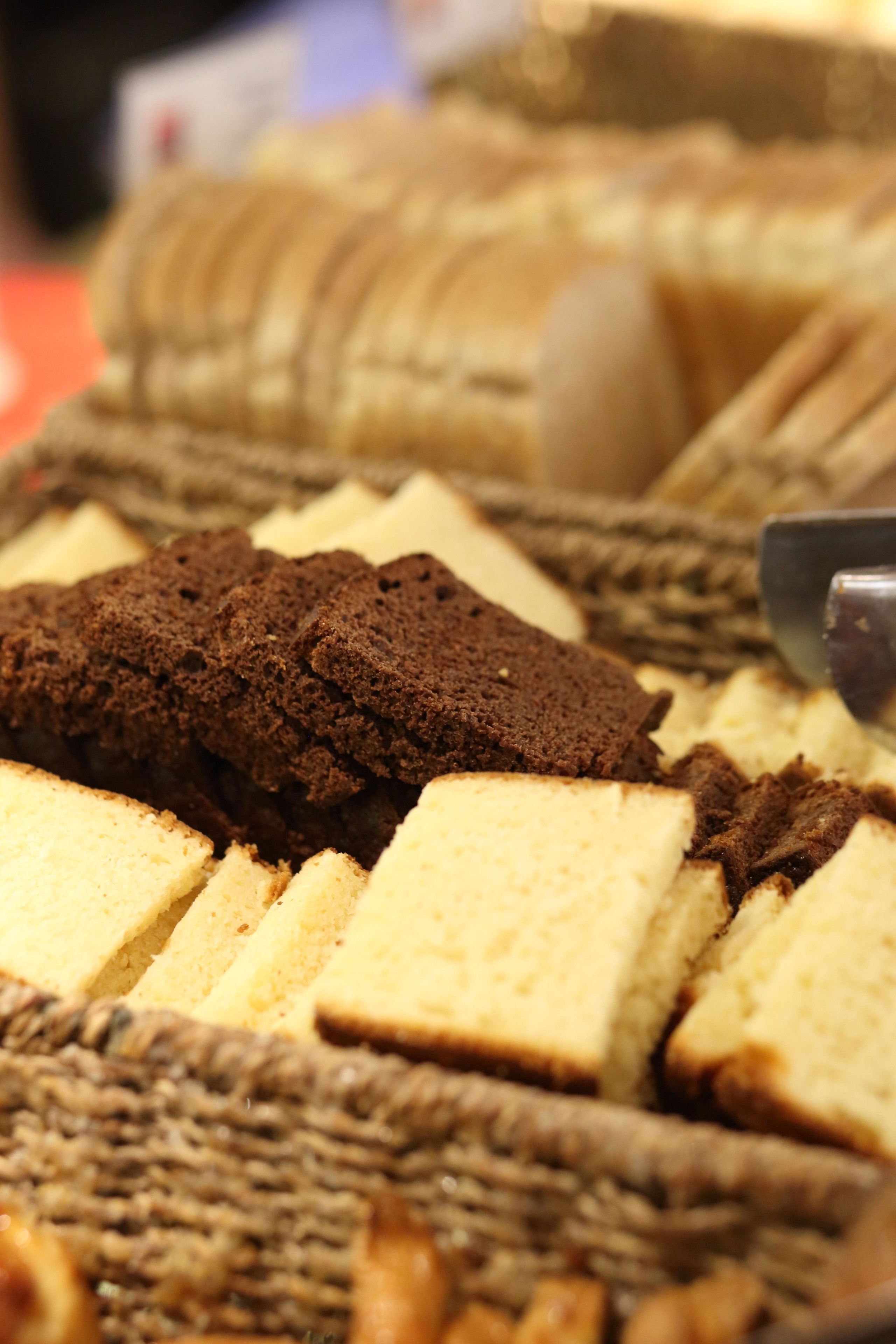 A close-up of a variety of cakes and pastries, including chocolate cake and sponge cake, arranged on a wicker surface.