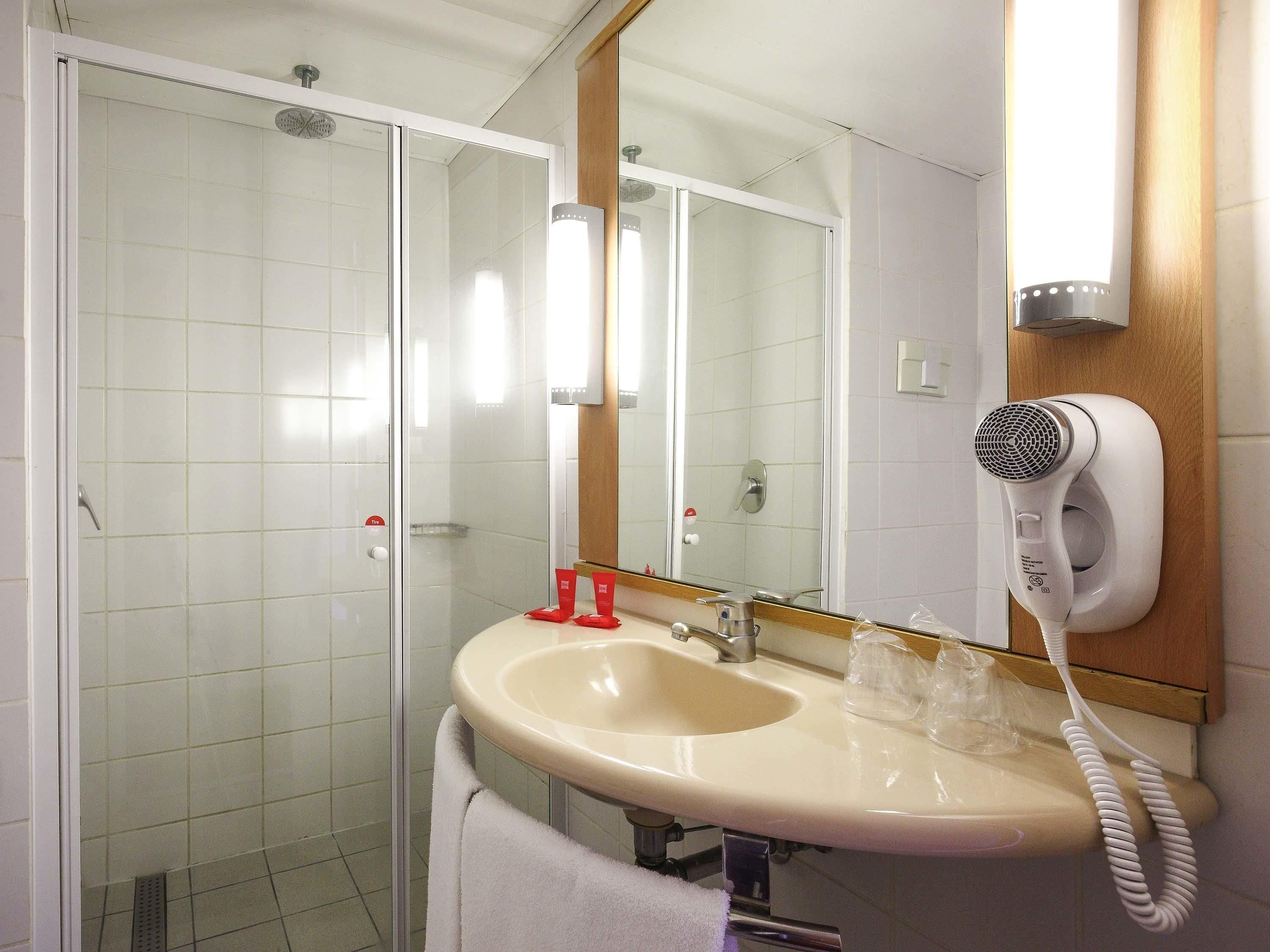 Un baño con lavamanos, espejo y un secador de pelo sujeto a la pared.