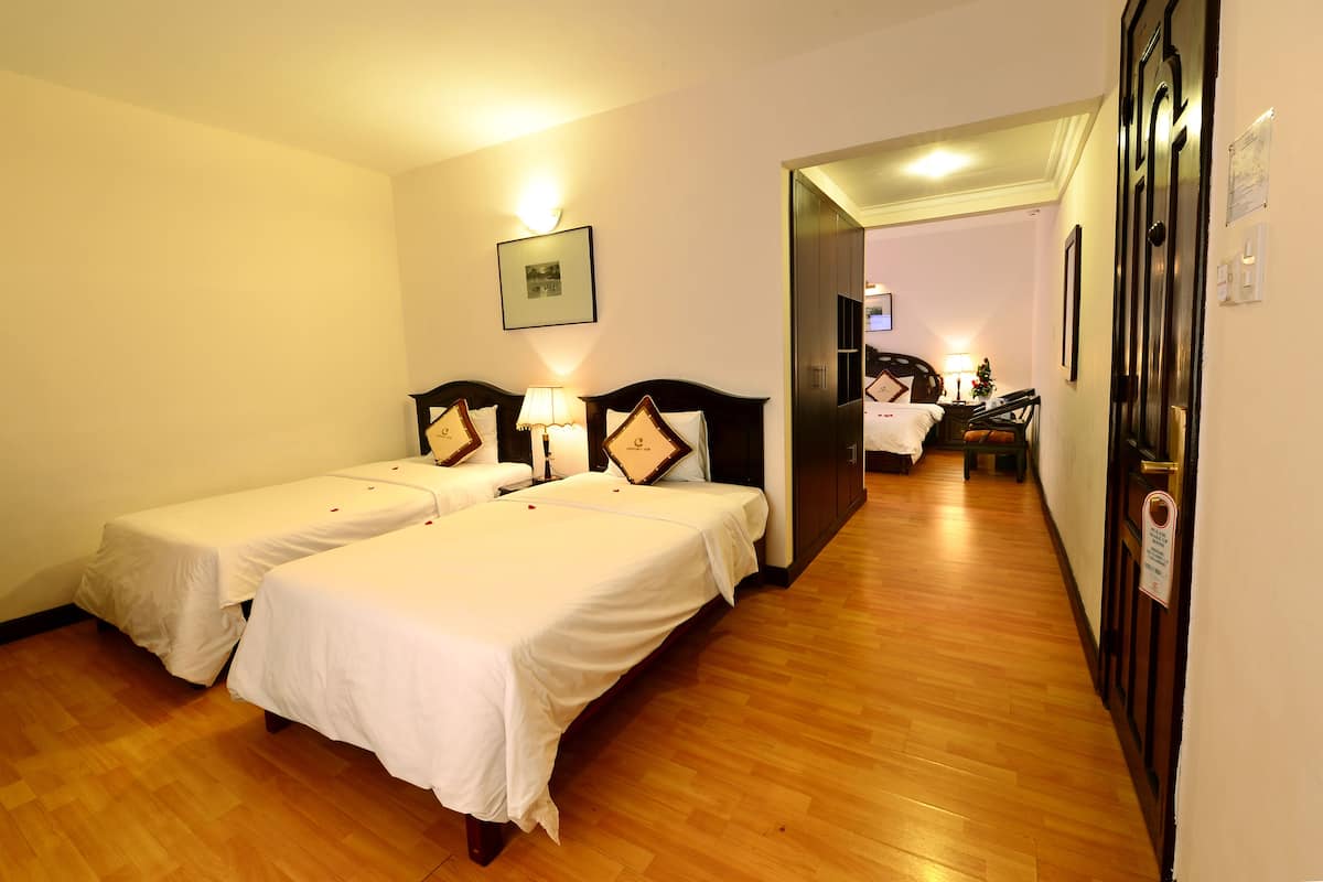 A hotel room with two single beds, wooden flooring, a small desk with a chair, and a television.