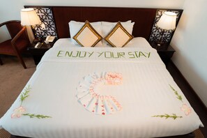 A hotel room with a neatly made bed, two decorative pillows, a bedside table with a lamp, and a chair.