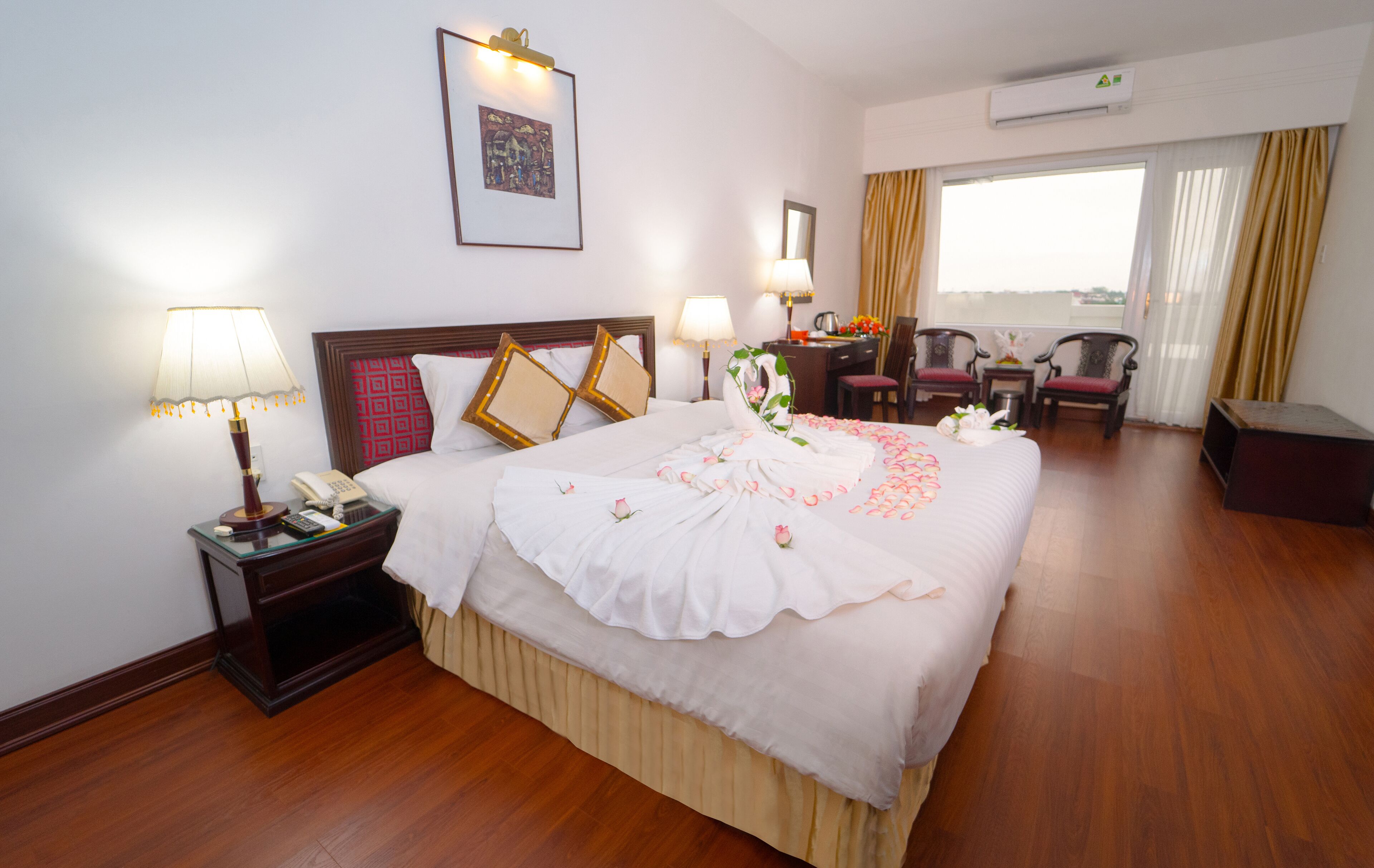 A hotel room with a large bed, bedside tables, a desk, two chairs, and a view of the outdoors.