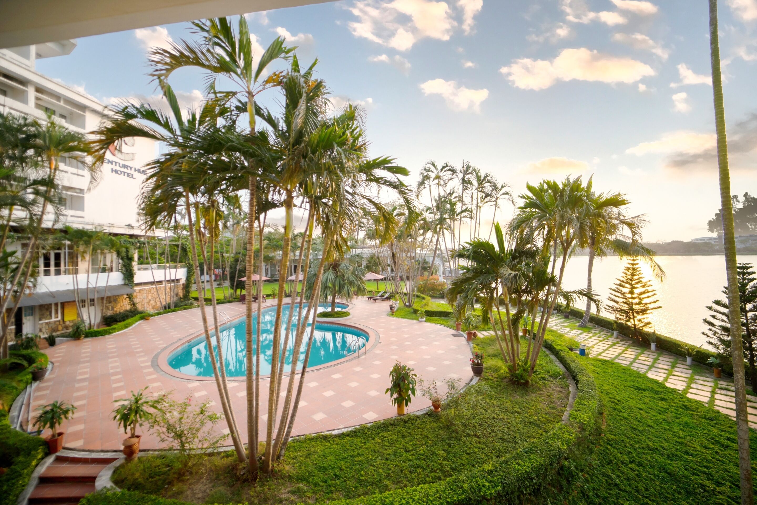 A pool area with palm trees and a view of the sea.