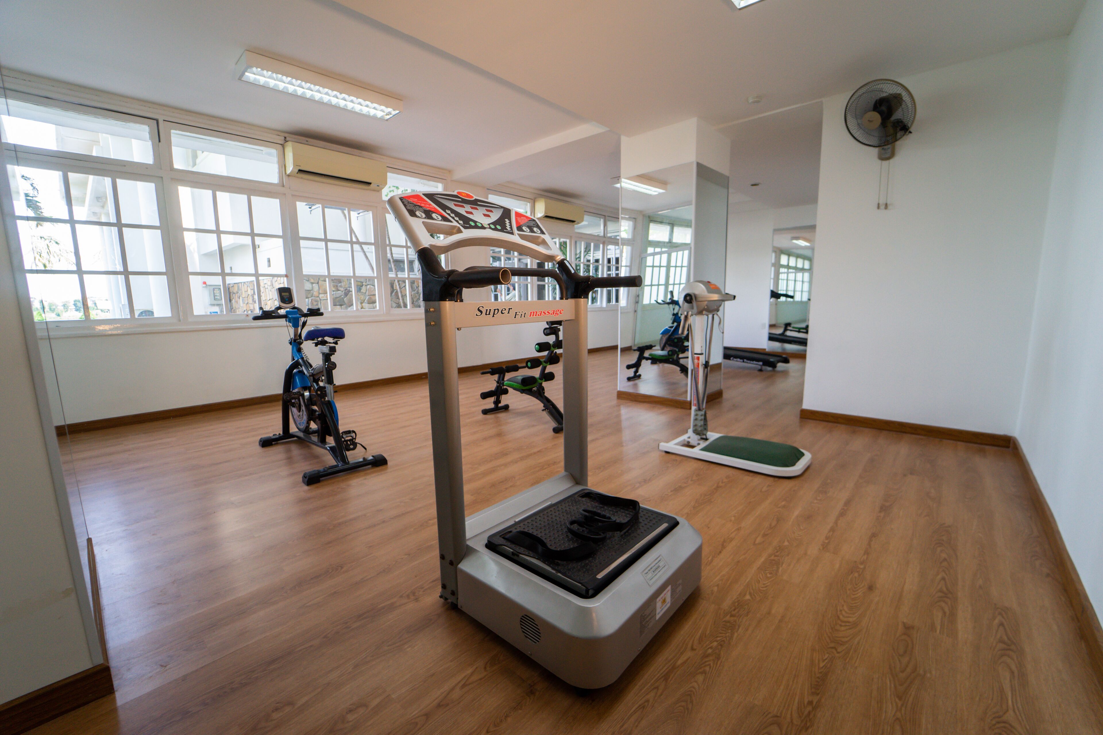 A gym with exercise equipment, large windows, and wooden floors.