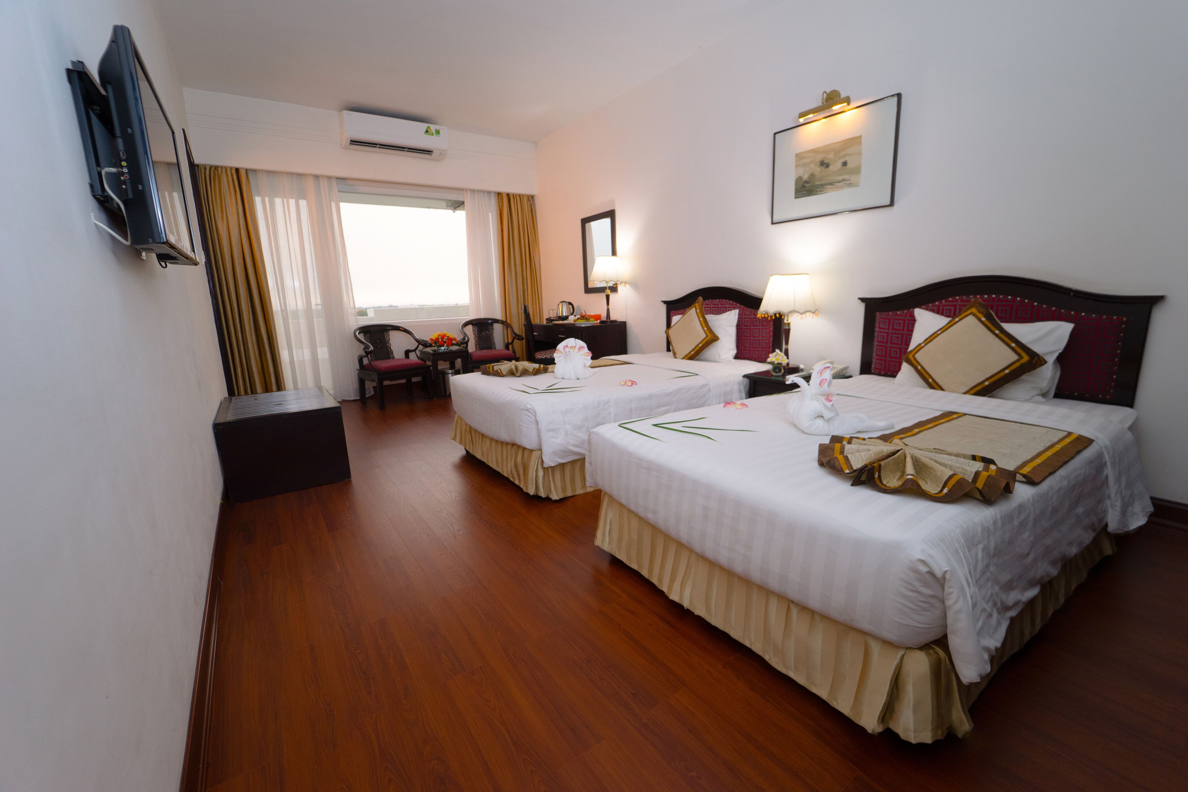 A hotel room with two beds, a desk, a chair, a TV, and an air conditioning unit.