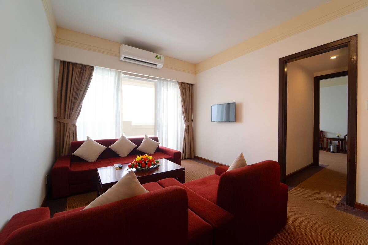 A hotel room with a red sofa set, a coffee table with flowers, and a flat-screen TV on the wall.