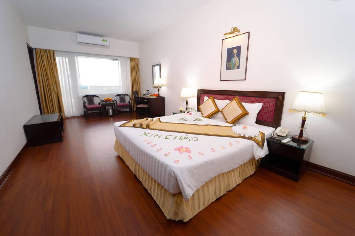 A hotel room with a large bed, a desk, a chair, and a window with curtains.