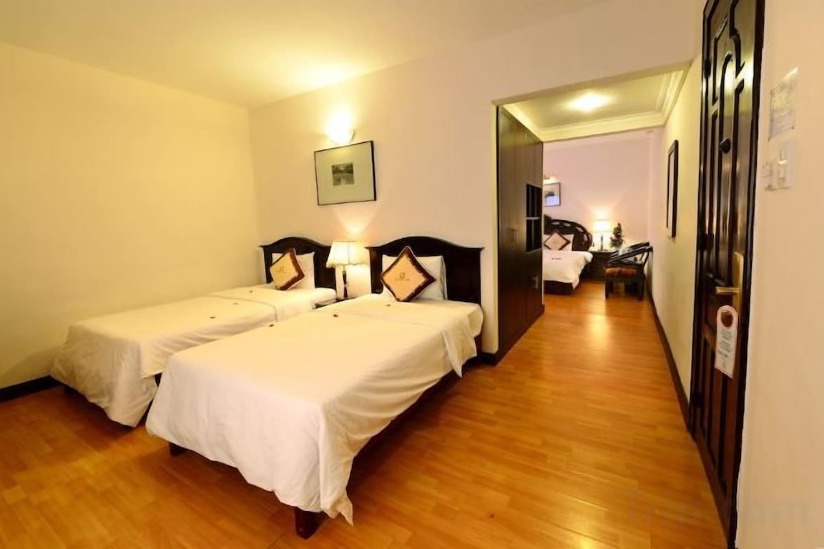 A hotel room with two beds, a wooden floor, a hallway, and a door leading to another room.