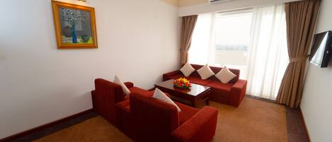 Habitación de hotel con un sofá rojo, una mesita de centro con flores, un cuadro en la pared y un equipo de aire acondicionado.