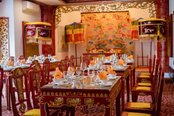 A banquet hall with long tables set for a formal event, adorned with traditional decorations and red and gold furniture.