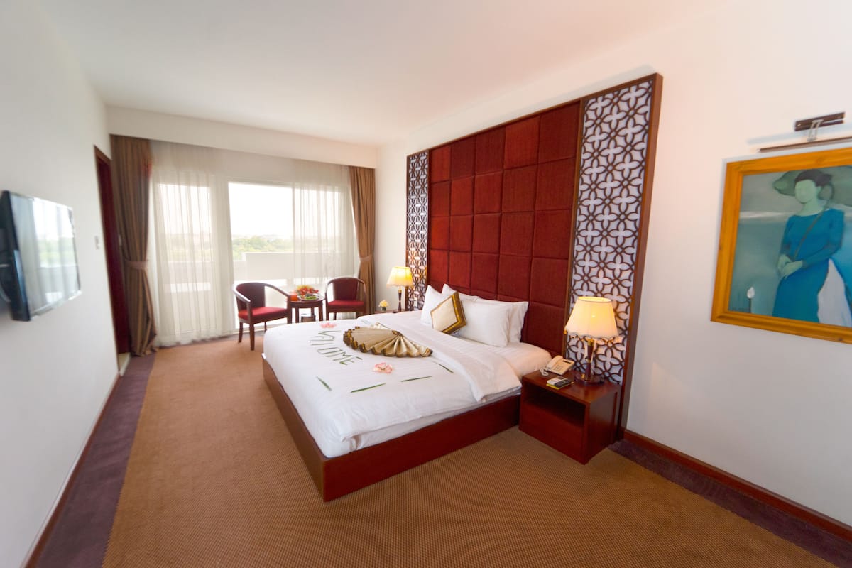 A hotel room with a large bed, two bedside tables, a chair, a desk, and a television.