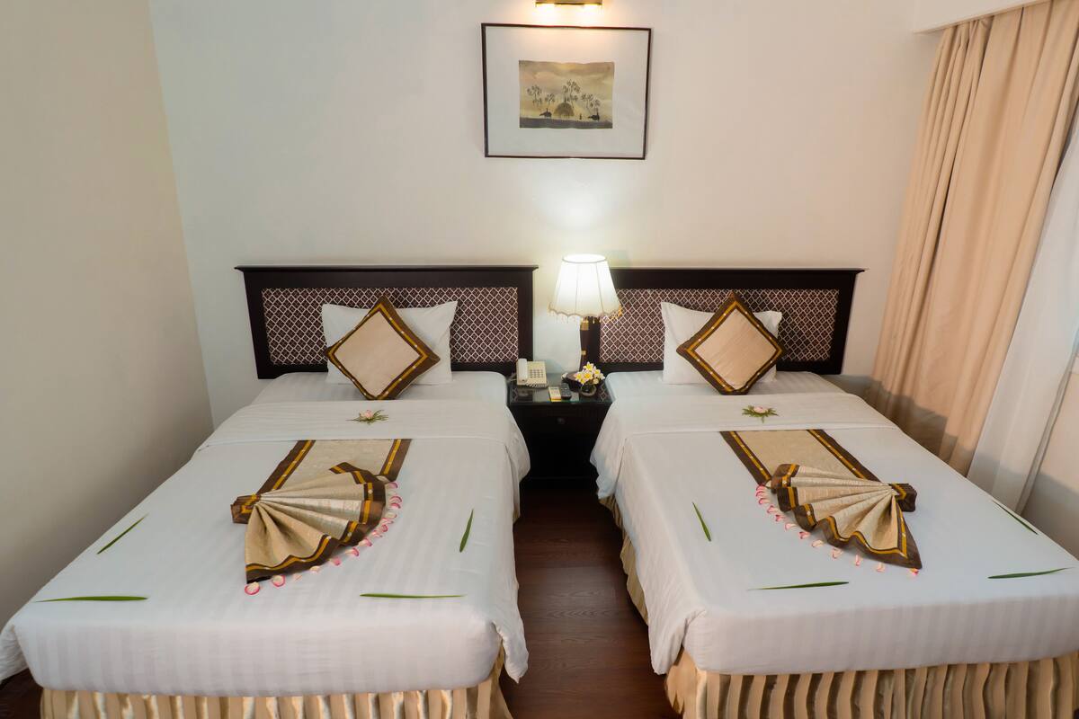 A hotel room with two beds, a nightstand with a lamp, a framed picture on the wall, and a window with curtains.