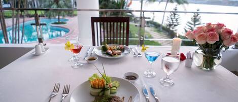 Una mesa de comedor con comida, cubiertos y una vela, con vista a una piscina y palmeras.