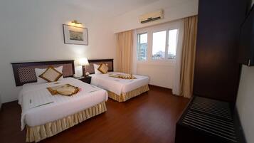 Hotelkamer met twee bedden, een nachtkastje met lamp, een airconditioningapparaat, een raam met gordijnen en een televisie.