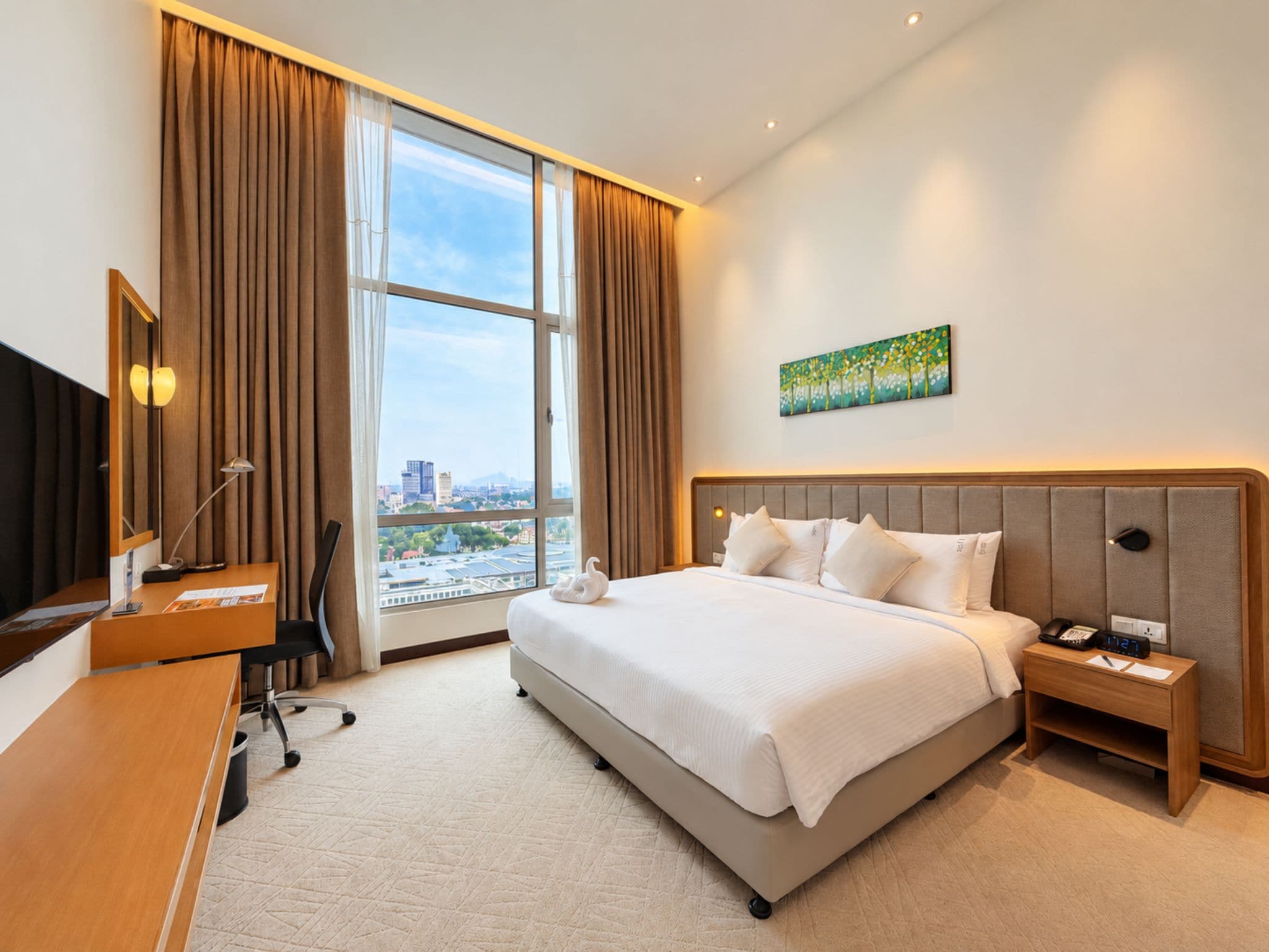 Ein Hotelzimmer mit einem großen Bett, einem Schreibtisch, einem Sessel, einem Fernseher, einem Gemälde und Blick auf die Stadt.