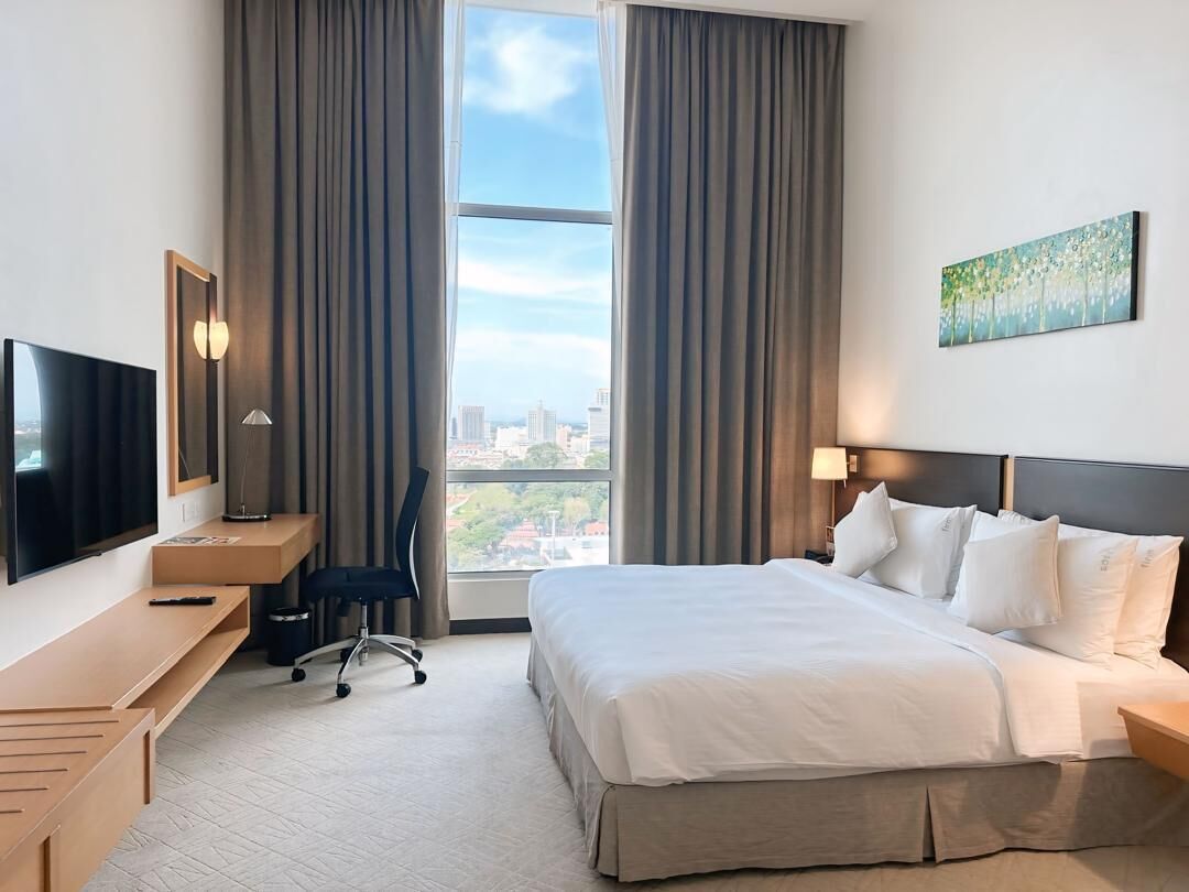 A hotel room with a bed, a desk, a chair, a TV, and a window with curtains.