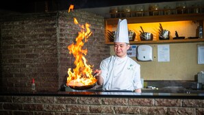 Ein Koch führt flambiertes Fertigstellen mit einer Pfanne über einem Kamin aus Ziegeln durch.