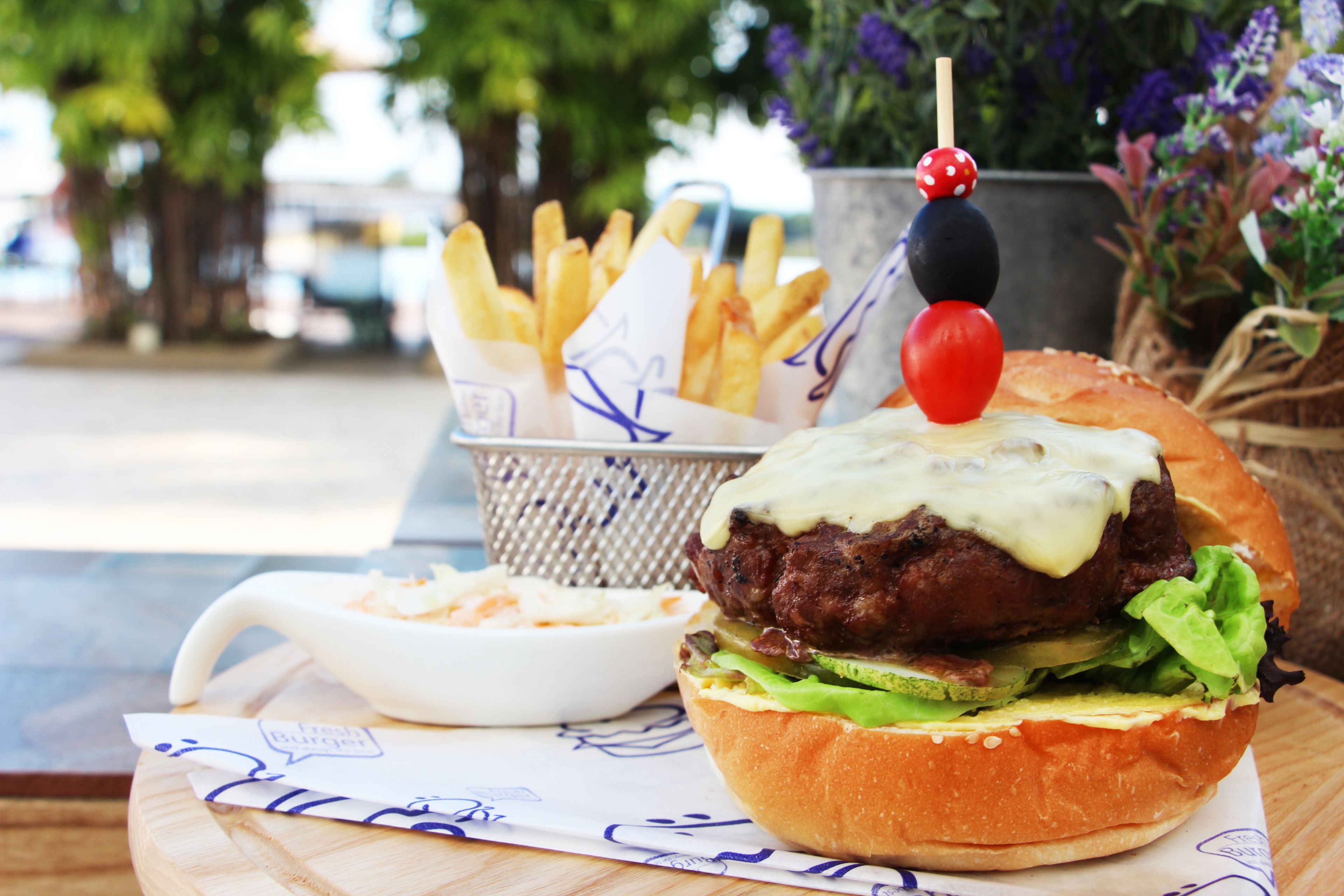 A burger with a side of fries and a small bowl of coleslaw on a wooden table.