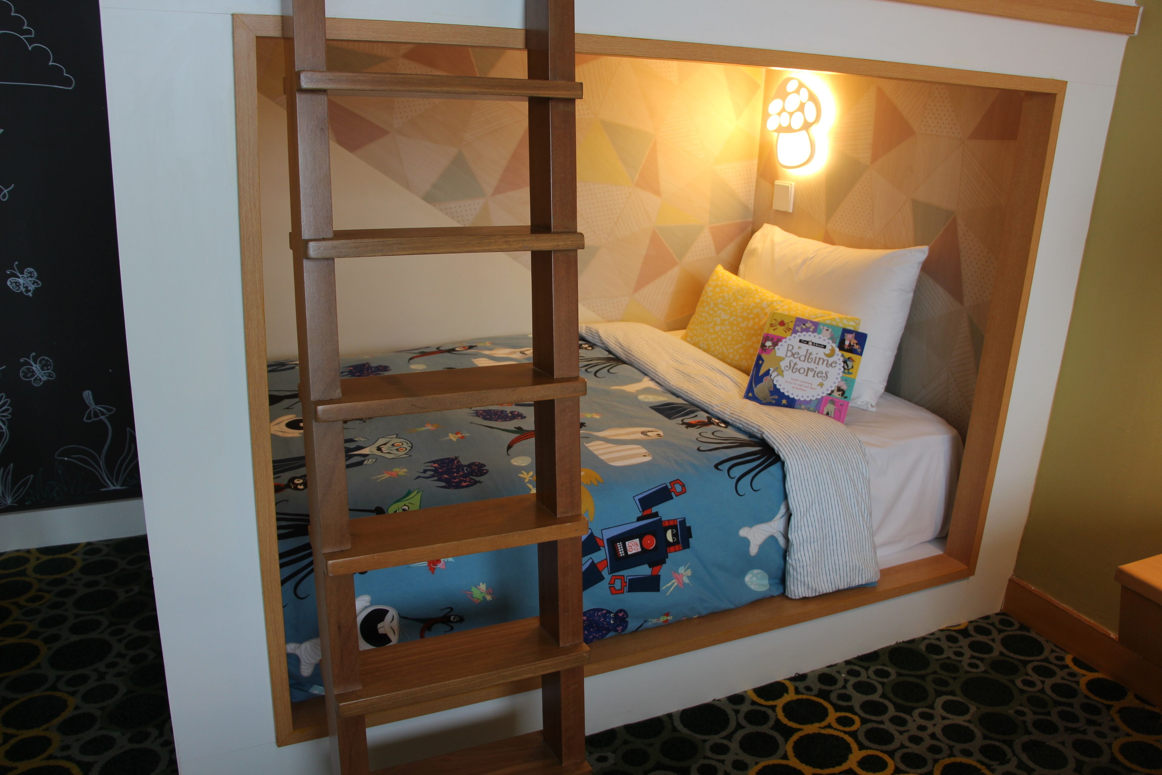 Une chambre confortable avec un lit intégré, une échelle et un luminaire fixé au mur.