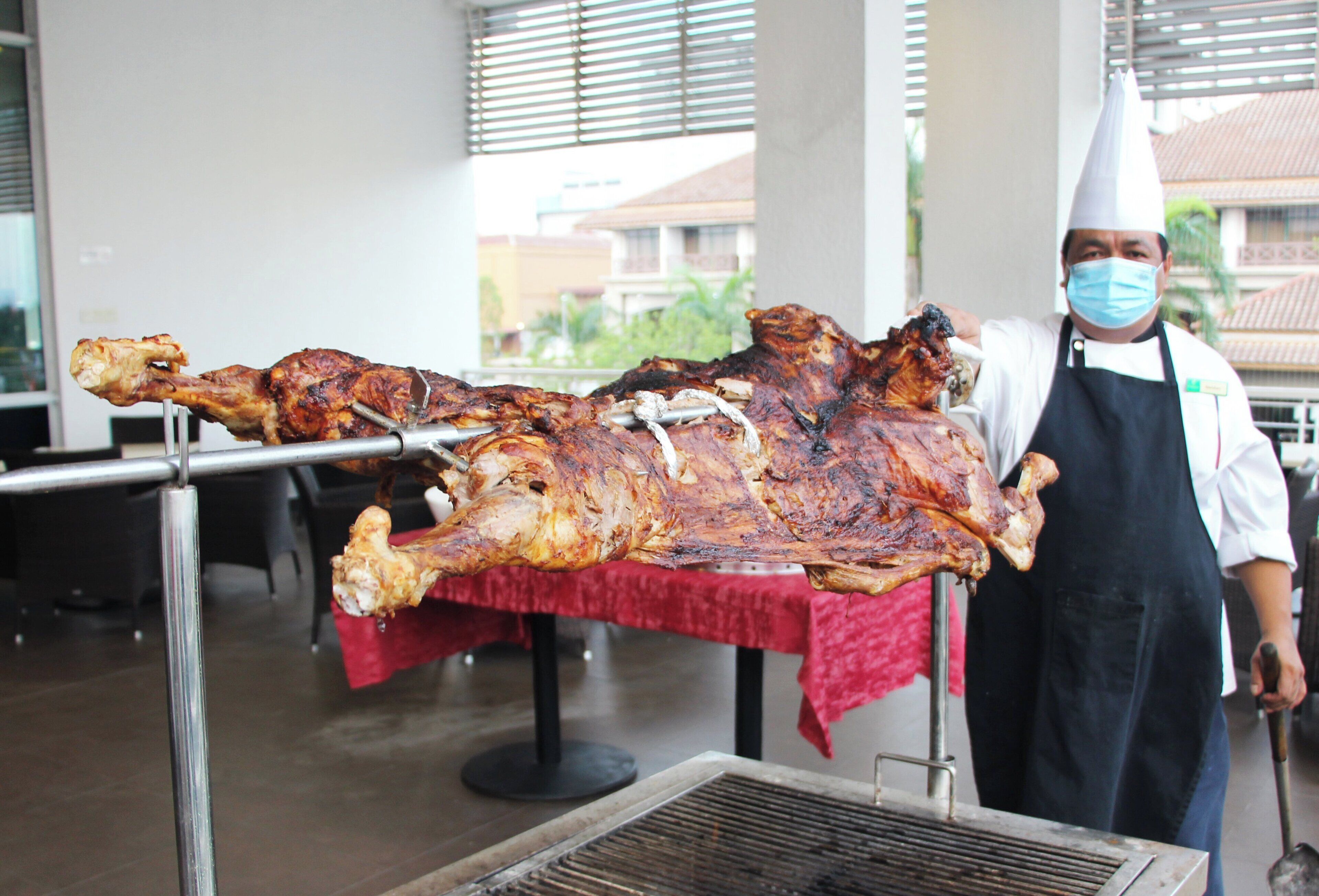 A large roasted pig on a spit, a person in a chef's uniform, and a grill in a restaurant setting.