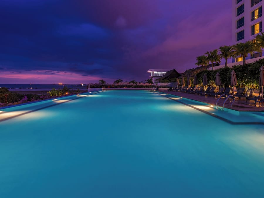 A swimming pool at twilight with lounge chairs and palm trees.