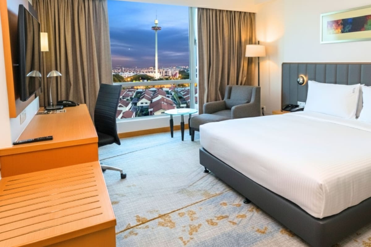 Ein Hotelzimmer mit einem großen Bett, einem Schreibtisch, einem Sessel und Blick auf eine Stadtlandschaft mit einem Turm.