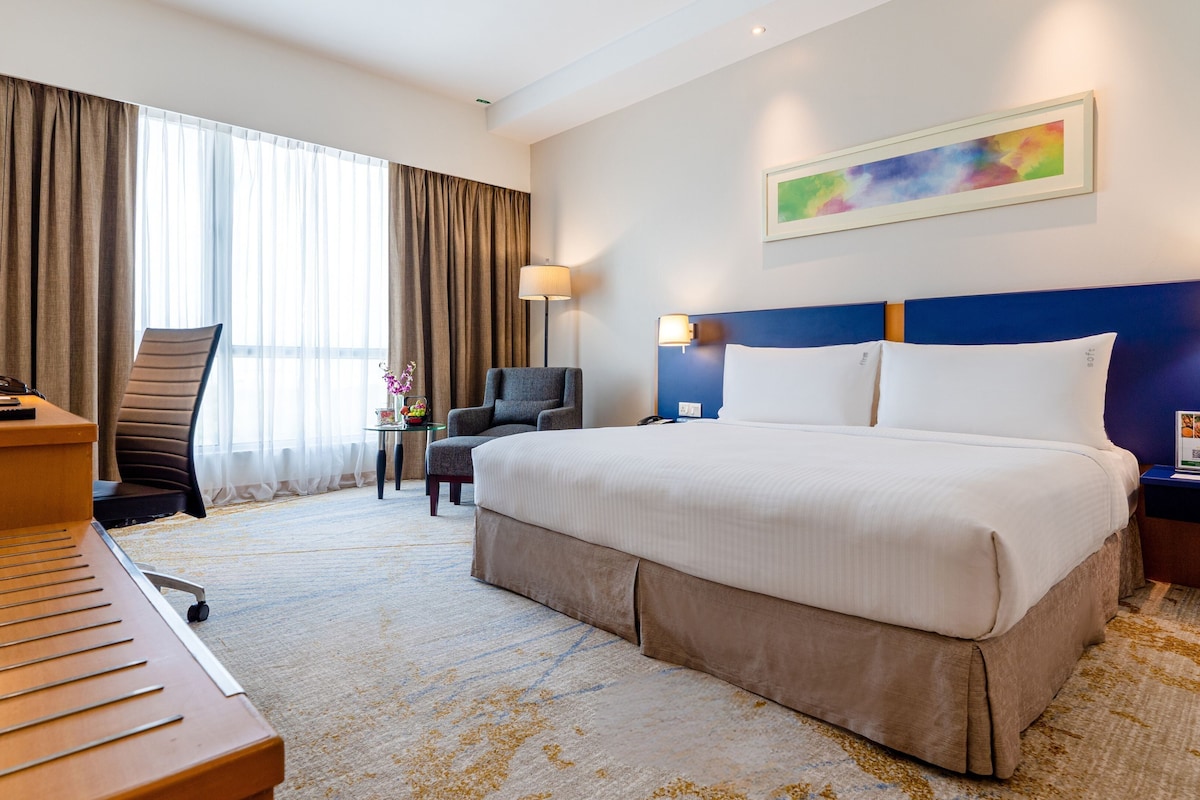Ein Hotelzimmer mit einem großen Bett, einem Schreibtisch mit Stuhl, einem Fernseher und einer Schreibtischlampe.