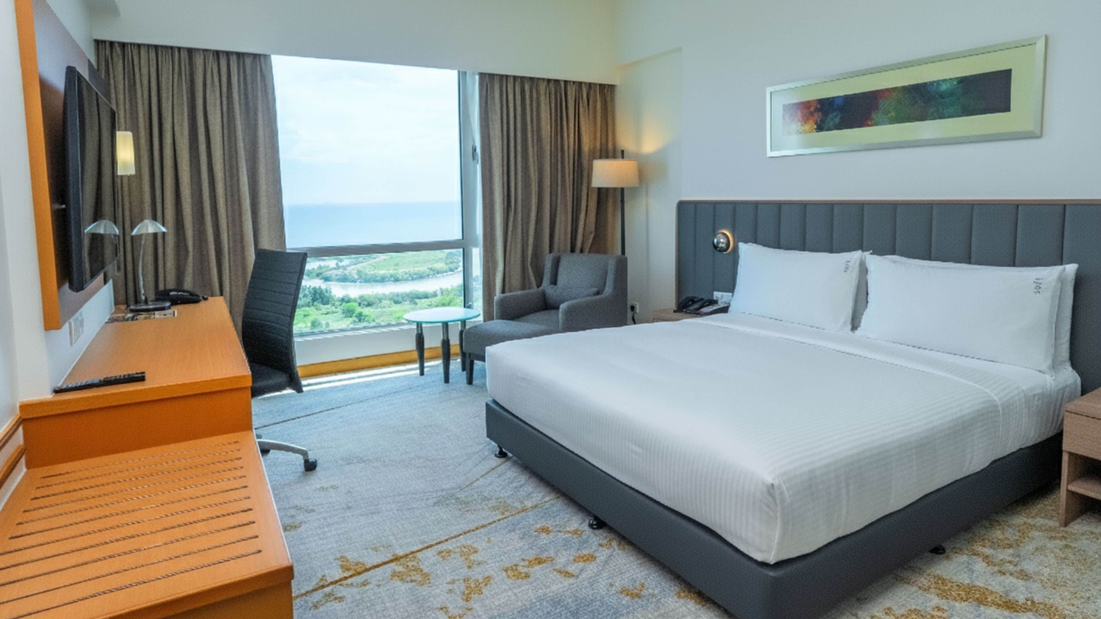Habitación de hotel con una cama grande, un escritorio, una silla, un televisor y ventana con vistas.