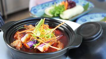 Una olla negra con tapa, que contiene un plato con carne, verduras y una salsa oscura.