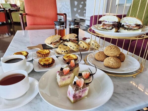 A table with pastries, sandwiches, and coffee cups.