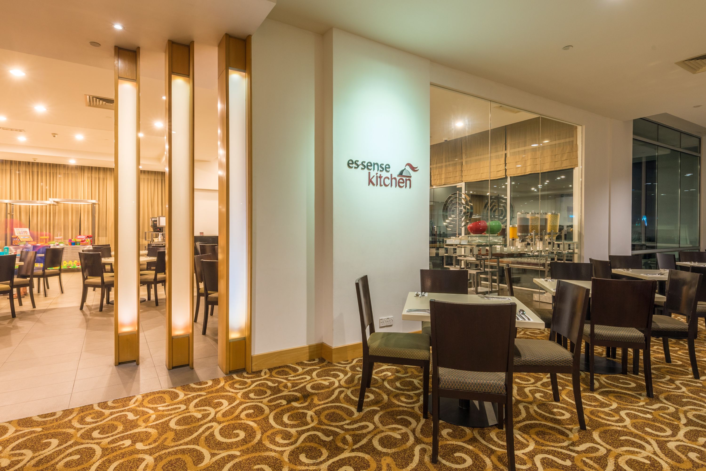 Un restaurant moderne, doté d’un intérieur épuré et bien éclairé, avec un tapis à motifs, des chaises en bois et une cloison en verre.