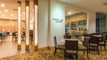 A modern restaurant with a clean, well-lit interior, featuring a patterned carpet, wooden chairs, and a glass partition wall.